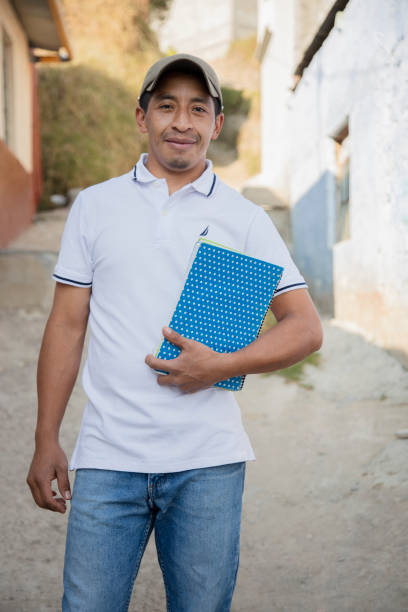 Hispanic father with notebooks outside school in rural area - Mayan adult man ready to go to study - Latin teacher in town